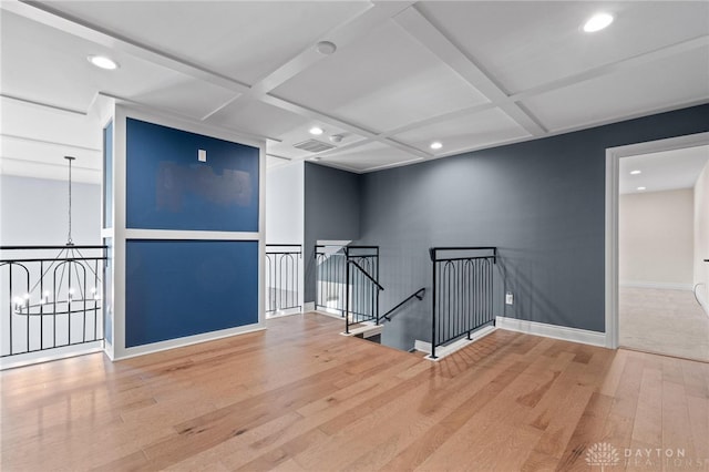 empty room featuring coffered ceiling, a notable chandelier, and wood-type flooring