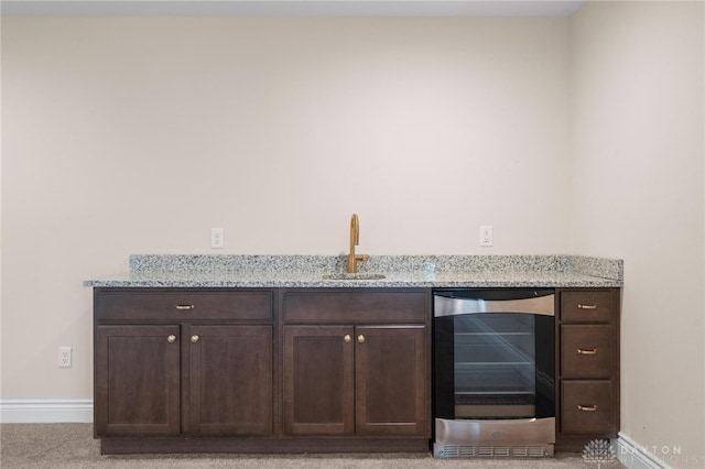 bar featuring light stone countertops, light carpet, sink, dark brown cabinets, and wine cooler