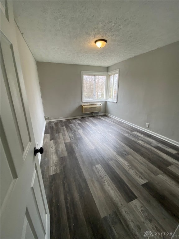 spare room with a textured ceiling, dark wood-type flooring, and a wall unit AC