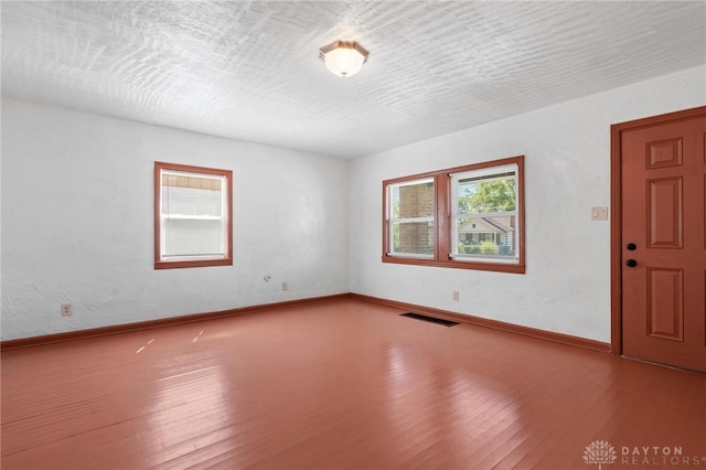 empty room with wood-type flooring, a wealth of natural light, and a textured ceiling