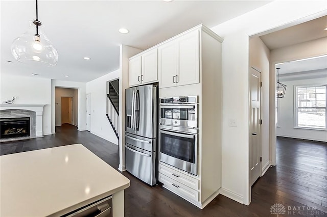 kitchen with dark wood-type flooring, white cabinetry, decorative light fixtures, stainless steel appliances, and a premium fireplace