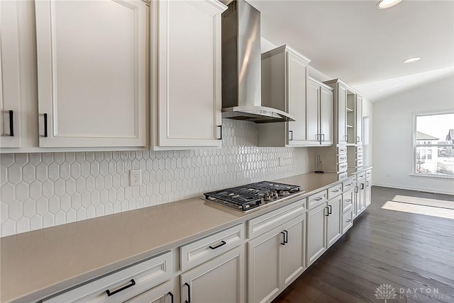 kitchen with dark wood-type flooring, stainless steel gas cooktop, white cabinetry, vaulted ceiling, and wall chimney range hood