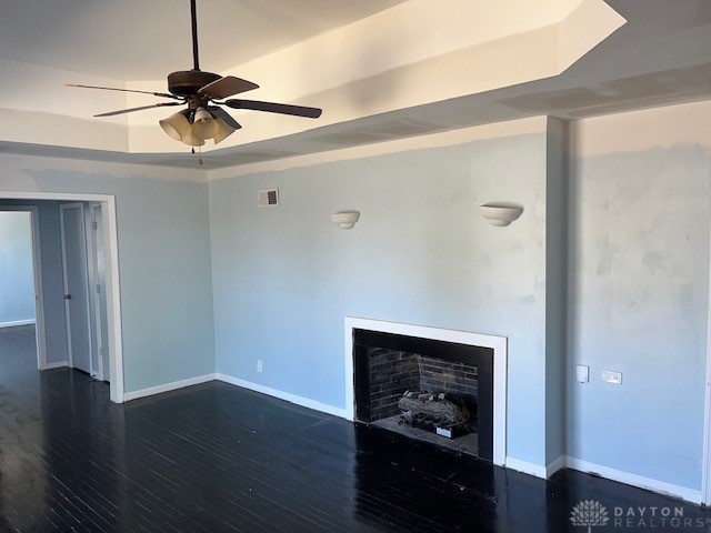 unfurnished living room featuring dark hardwood / wood-style flooring, a raised ceiling, and ceiling fan