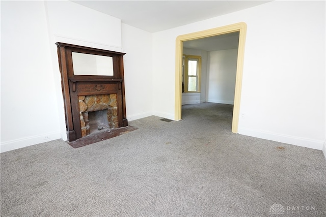 unfurnished living room with a stone fireplace and carpet flooring