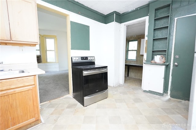 kitchen featuring light brown cabinetry, a healthy amount of sunlight, stainless steel electric range, and light carpet