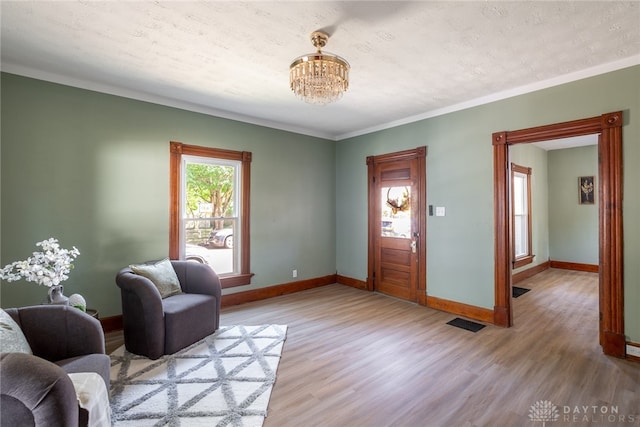 foyer with an inviting chandelier, light hardwood / wood-style floors, ornamental molding, and a textured ceiling