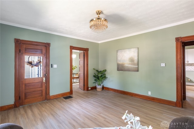 entrance foyer featuring light wood-type flooring, crown molding, and an inviting chandelier