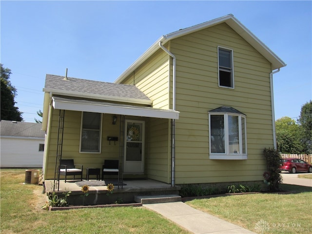 view of front facade featuring central AC unit, covered porch, and a front yard