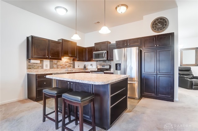 kitchen with a kitchen breakfast bar, a center island, stainless steel appliances, decorative backsplash, and light colored carpet