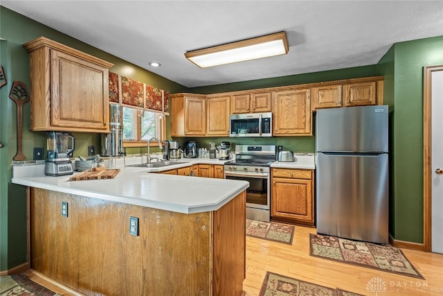 kitchen with a textured ceiling, light hardwood / wood-style flooring, stainless steel appliances, sink, and kitchen peninsula