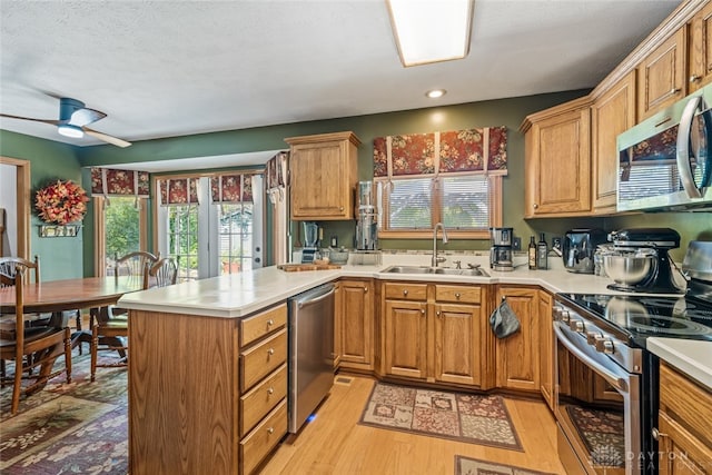 kitchen featuring light wood-type flooring, kitchen peninsula, sink, ceiling fan, and appliances with stainless steel finishes