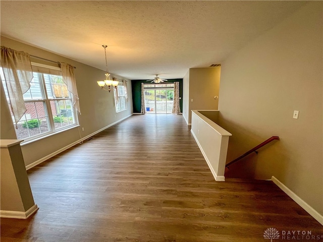 unfurnished dining area featuring a wealth of natural light, dark wood-type flooring, a textured ceiling, and an inviting chandelier