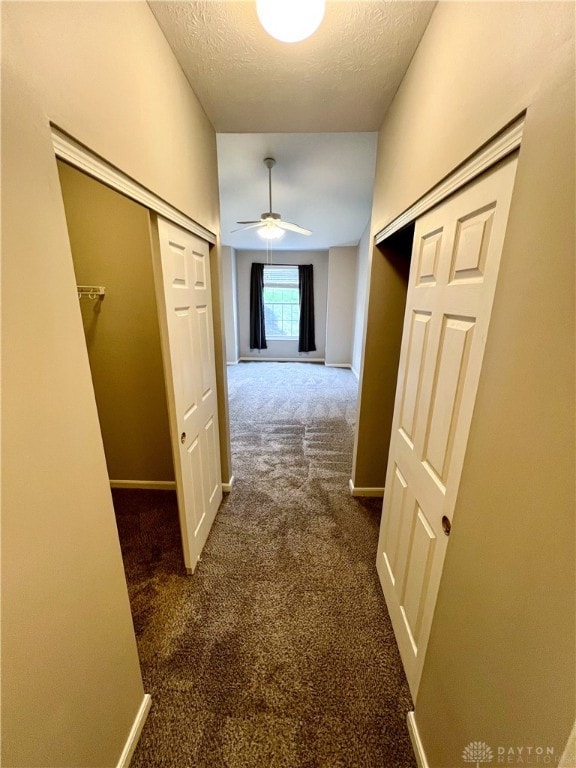 hall with a textured ceiling and dark colored carpet