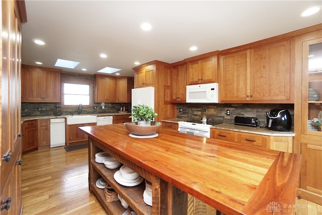 kitchen featuring light wood-type flooring, white appliances, a skylight, butcher block countertops, and sink