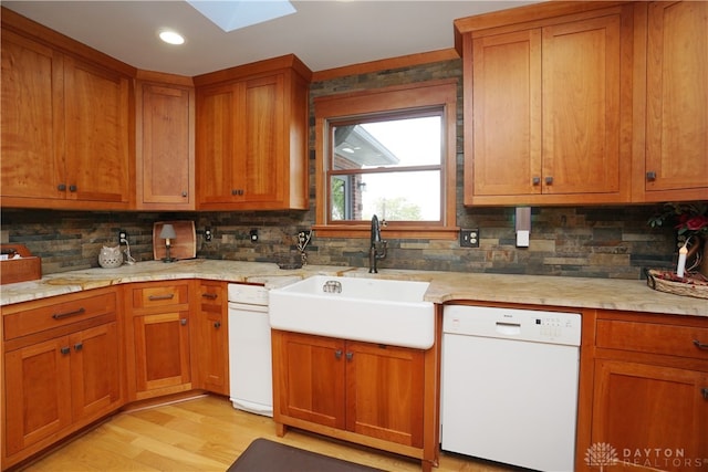 kitchen featuring a skylight, white dishwasher, light wood-type flooring, light stone countertops, and sink