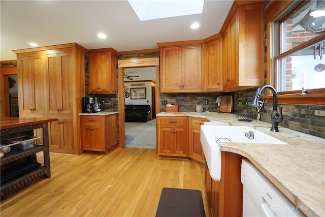 kitchen with a skylight, backsplash, white dishwasher, light wood-type flooring, and sink