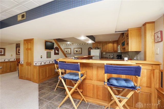 kitchen featuring dark tile patterned flooring, kitchen peninsula, fridge, decorative backsplash, and wooden walls