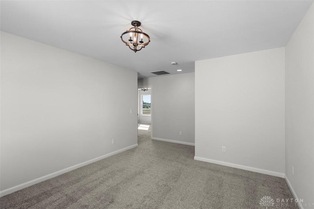 carpeted empty room with a chandelier, visible vents, and baseboards