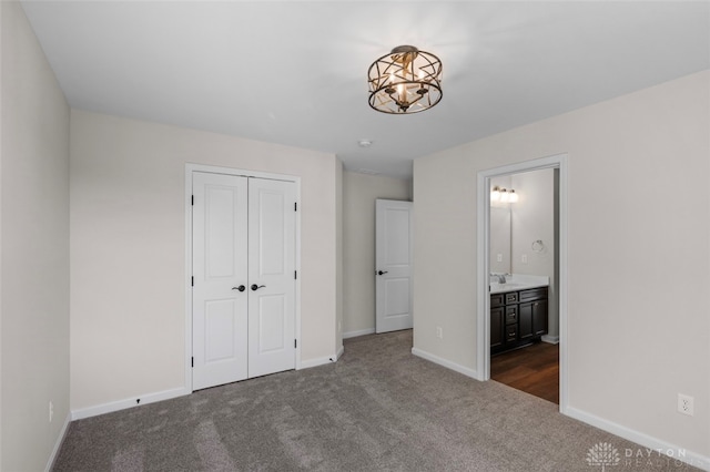 unfurnished bedroom featuring dark carpet, a notable chandelier, a closet, and ensuite bathroom