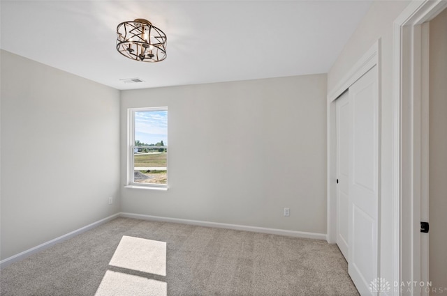 unfurnished bedroom featuring light colored carpet, a notable chandelier, and a closet