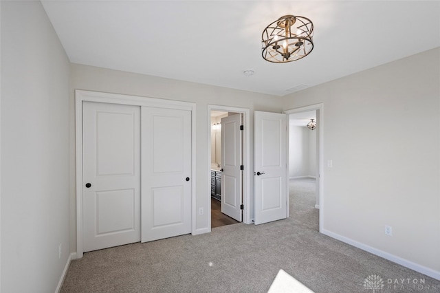 unfurnished bedroom with a closet, a notable chandelier, ensuite bath, and carpet floors