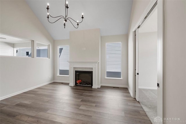 unfurnished living room featuring a chandelier, high vaulted ceiling, a premium fireplace, wood finished floors, and baseboards