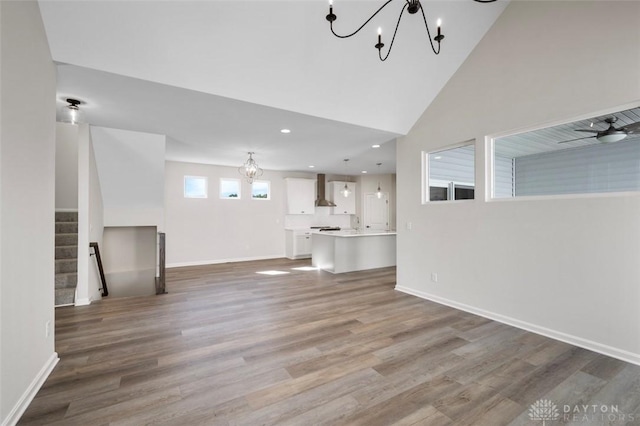 unfurnished living room with ceiling fan with notable chandelier, stairway, baseboards, and wood finished floors