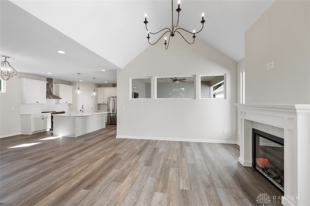 unfurnished living room featuring a premium fireplace, ceiling fan with notable chandelier, light hardwood / wood-style flooring, and high vaulted ceiling