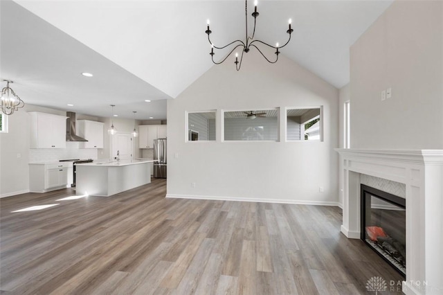 unfurnished living room featuring light wood-type flooring, baseboards, a notable chandelier, and a glass covered fireplace