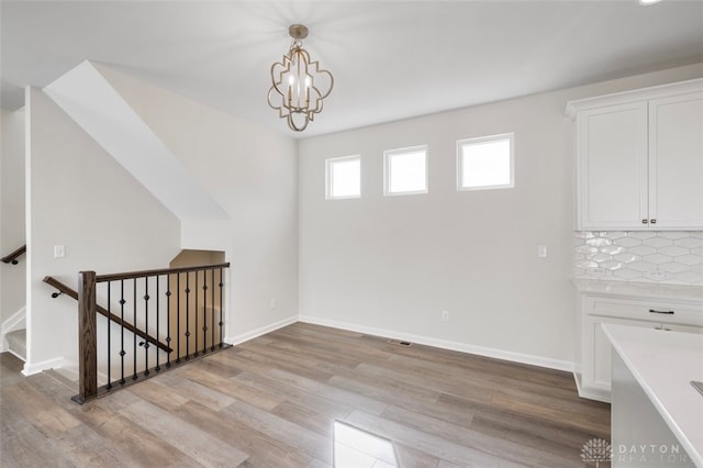 unfurnished dining area featuring an inviting chandelier and light hardwood / wood-style floors