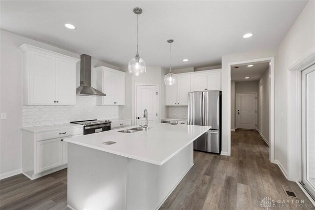 kitchen with appliances with stainless steel finishes, sink, wall chimney range hood, an island with sink, and dark wood-type flooring