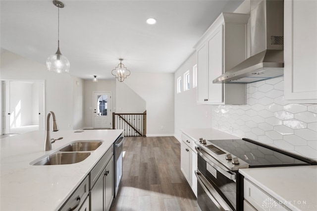 kitchen with wall chimney exhaust hood, hanging light fixtures, stainless steel appliances, sink, and hardwood / wood-style flooring