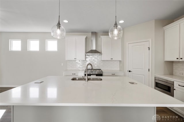 kitchen with tasteful backsplash, stainless steel appliances, wall chimney exhaust hood, and an island with sink