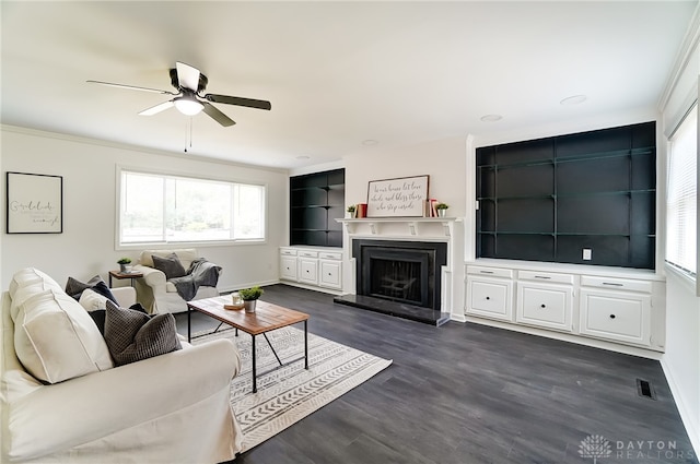 living room featuring built in features, crown molding, ceiling fan, and dark hardwood / wood-style flooring