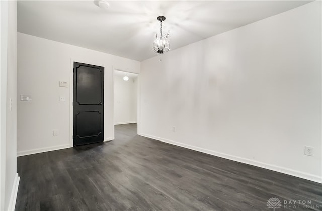 spare room with dark wood-type flooring and a notable chandelier