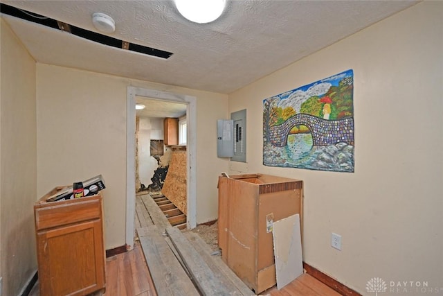 hallway with electric panel, a textured ceiling, and light wood-type flooring