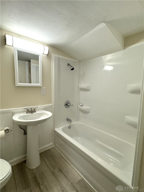 bathroom featuring a textured ceiling,  shower combination, hardwood / wood-style floors, and toilet