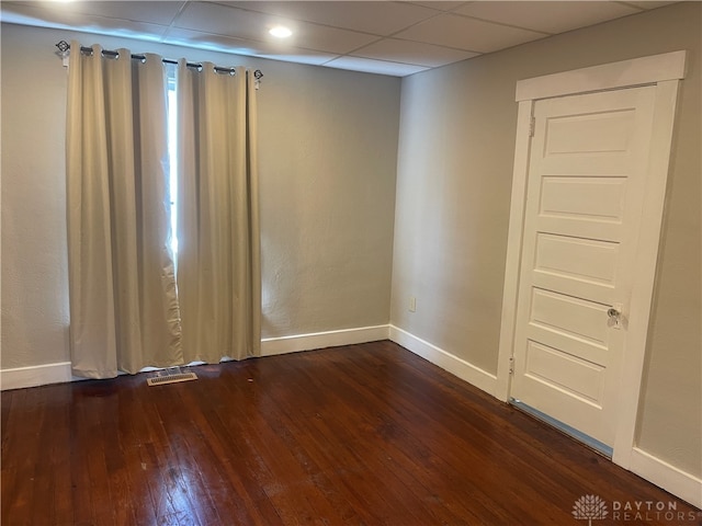 empty room with dark hardwood / wood-style flooring and a drop ceiling