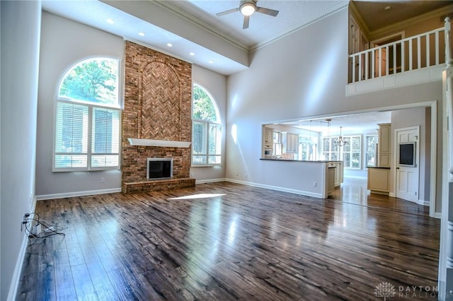 unfurnished living room featuring a high ceiling, a fireplace, dark hardwood / wood-style floors, ceiling fan, and crown molding