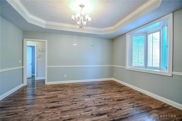 empty room with dark hardwood / wood-style floors, a raised ceiling, a textured ceiling, ornamental molding, and a chandelier