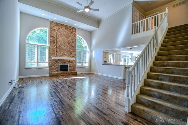 unfurnished living room featuring ceiling fan, a large fireplace, dark hardwood / wood-style flooring, a towering ceiling, and crown molding