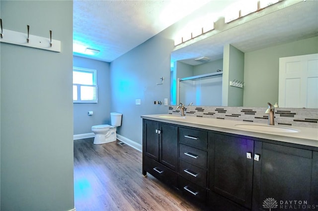 bathroom with toilet, a shower with door, backsplash, wood-type flooring, and vanity