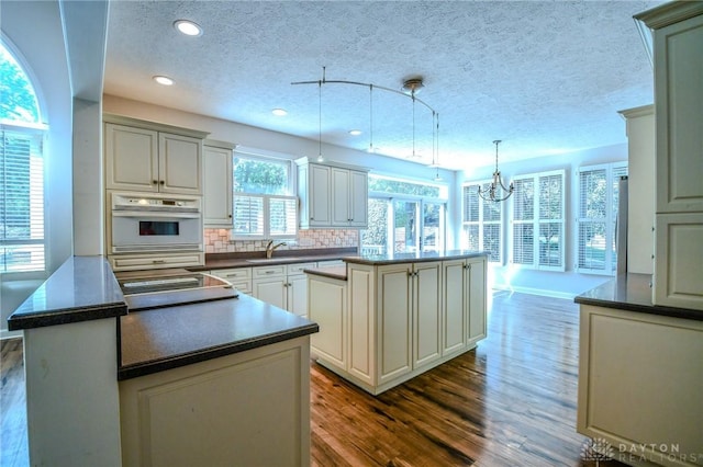 kitchen with tasteful backsplash, oven, a textured ceiling, pendant lighting, and a center island