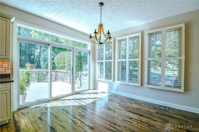 unfurnished dining area with dark wood-type flooring, plenty of natural light, an inviting chandelier, and a textured ceiling