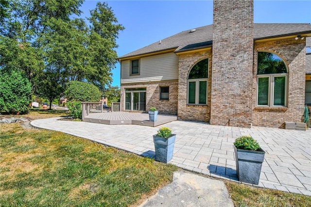 back of property featuring a wooden deck, a patio area, and a yard