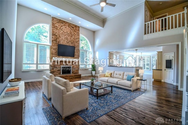 living room with ceiling fan, dark hardwood / wood-style floors, a fireplace, a towering ceiling, and ornamental molding