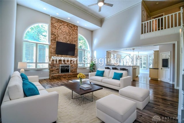 living room featuring ceiling fan, a fireplace, a high ceiling, crown molding, and hardwood / wood-style flooring