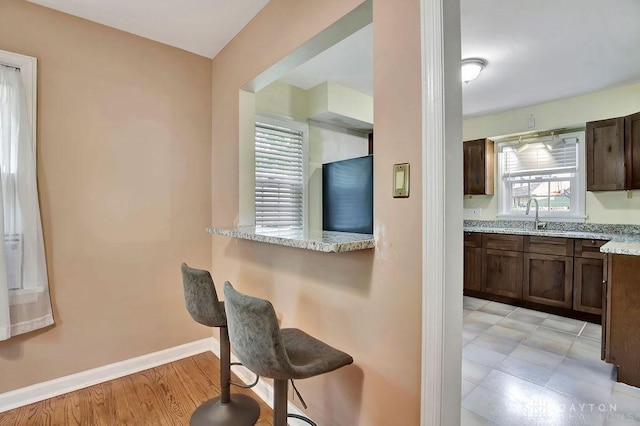 kitchen with light stone counters, refrigerator, light hardwood / wood-style flooring, a kitchen breakfast bar, and kitchen peninsula