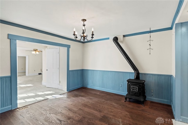 unfurnished dining area featuring hardwood / wood-style floors, ceiling fan with notable chandelier, a wood stove, and ornamental molding