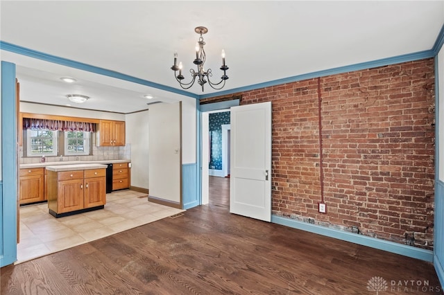 kitchen with brick wall, crown molding, decorative light fixtures, light hardwood / wood-style flooring, and a chandelier